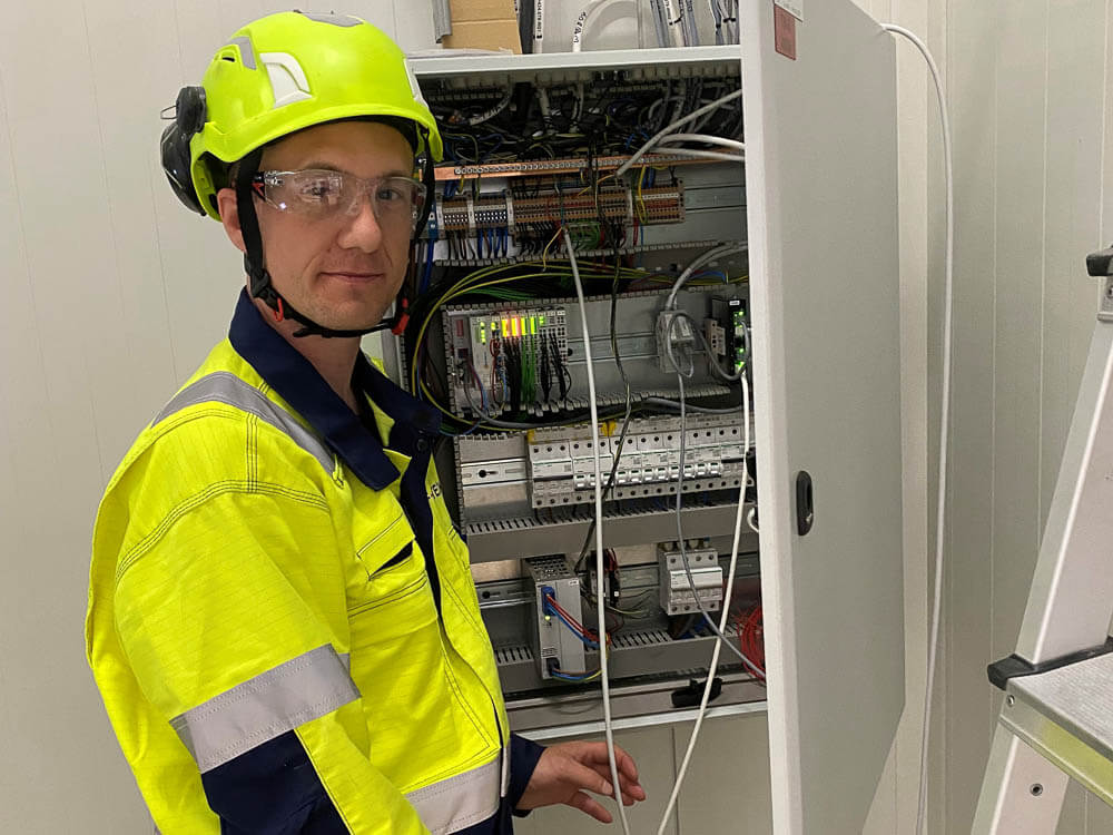 Aleksander Maubach i arbeidstøy med hjelm og vernebriller foran et åpent elektroskap