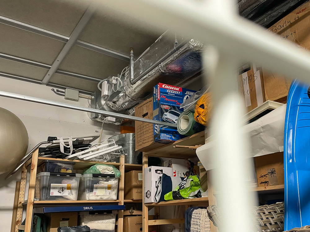 Et lite tilluftsaggregat i hjørnet på en kjelerbod med hyller fulle av turutstyr mm