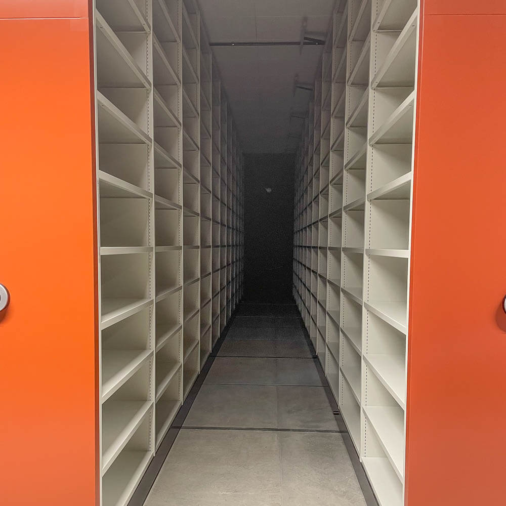 Tå åpne, hvite hyllereoler i magasinet, sett innover langs hyllene.