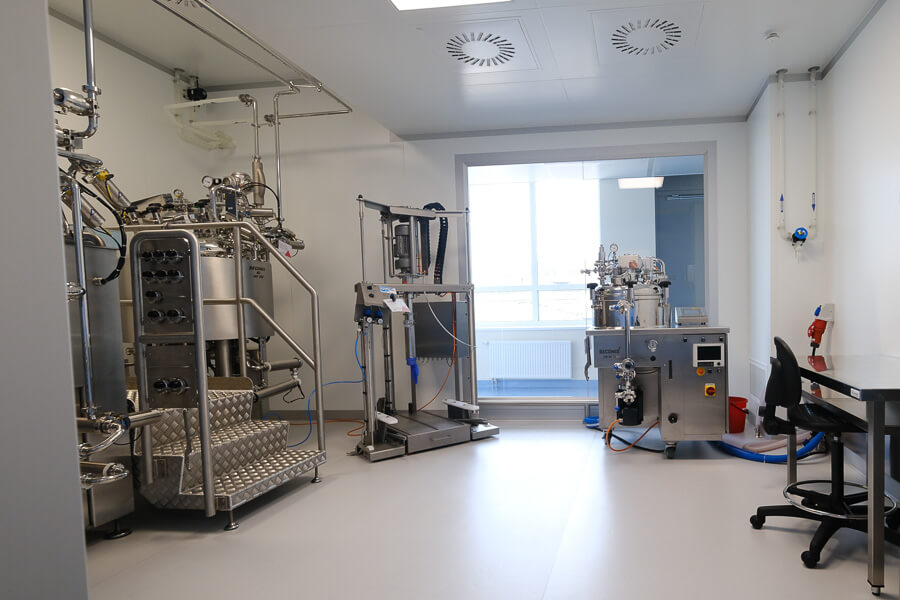 Renrom laboratorium med trapp mellom to store maskiner til venstre i bildet, en mindre rigg innerst til høyre og en pult med stol høet til høyre i bildet