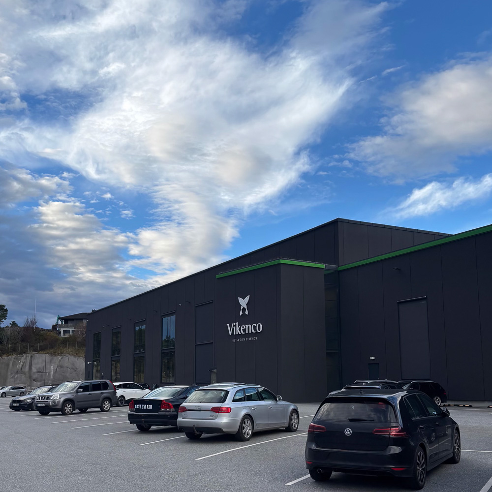 Mørkebrunt bygg med Vikenco-logo på veggen og biler i forgrunnen