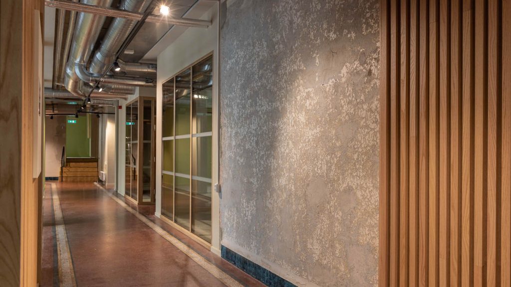 Bilde av korridor med glassvegg inn til møterom og ventilasjonskanaler i taket